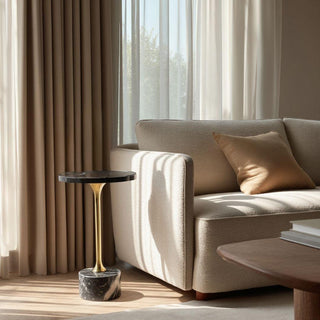 Black marble pedestal side table with brass stem styled beside a neutral sofa in soft natural light, showcasing an elevated quiet luxury living room moment with modern, sculptural appeal.