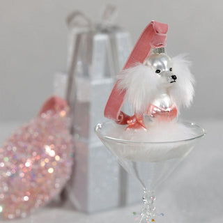 Decorative dog figure in a martini glass with a pink hat on a light gray background