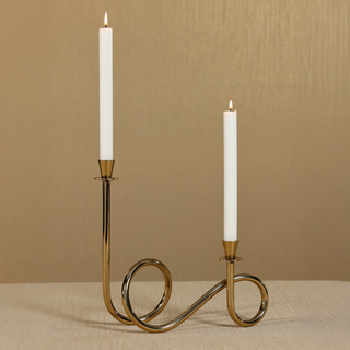 Polished gold Breda two-tier brass candle holder with white tapers styled on neutral surface in modern living room.