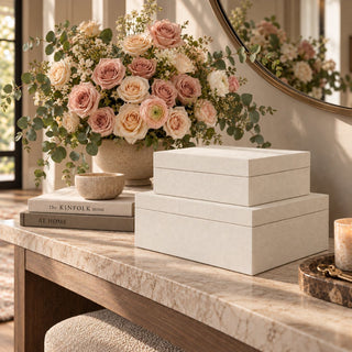 Set of two silk linen decorative boxes in a soft cream finish and graduated sizes, stacked on a stone console table with neutral books and blush florals in a warm modern entryway.