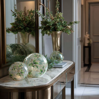 Set of holly and faux snow crackled glass LED globes with gold detailing displayed on marble console table in entryway with greenery and brass accents – elegant illuminated holiday décor with soft warm glow and built-in timer for refined winter styling.