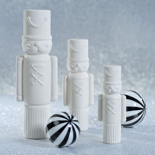 Set of matte white ceramic soldiers in varying sizes styled with black and white ornaments – minimalist Christmas display.