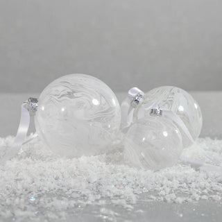 Set of white marbled glass ornaments with satin ribbons resting on snowy surface – elegant handcrafted holiday ornaments for neutral Christmas styling.