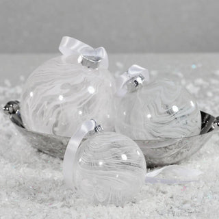 Set of white watercolor glass ball ornaments with satin bows arranged in silver bowl on snowy surface – handcrafted glass holiday décor for modern minimalist styling