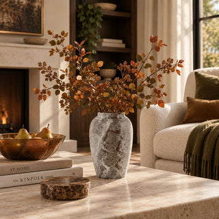 Small Tuscan vase with fall branches on a stone coffee table by a fireplace