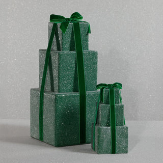 Small and large stack of green glittery gift boxes with ribbons on a gray background.
