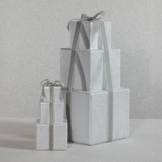 Small glittering silver stacked present décor with satin gray ribbon, styled in an elegant modern winter vignette.