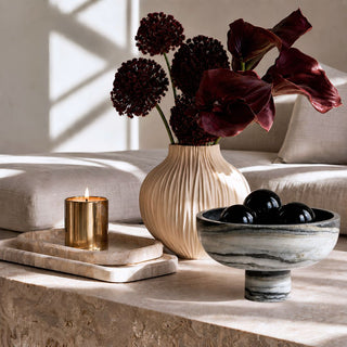 Black and white swirled marble pedestal bowl styled with black crystal fill balls on a stone coffee table beside burgundy florals and cream decor.