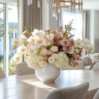 Elegant faux floral centerpiece with 27" real touch creamy white orchids, blush roses, and hydrangeas in a white ceramic vase on a modern dining table