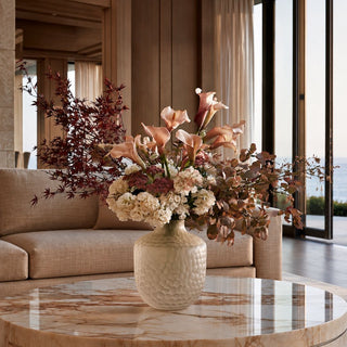 Faceted taupe brown frosted cut glass vase styled with a large fall inspired floral arrangement on a marble coffee table in a modern coastal home with ocean views