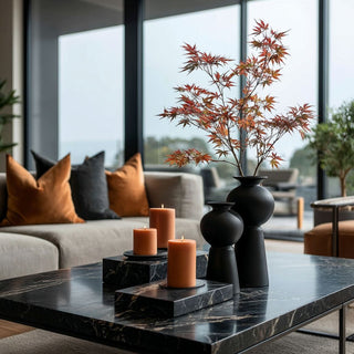 Styled Hinoki Matte Black vase in two sizes with autumn branches styled alongside black marble coffee table and rust candles in modern living room.