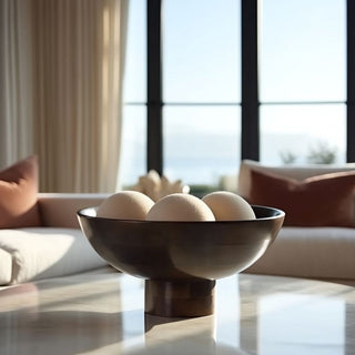 Large pedestal mango wood bowl filled with decorative spheres, styled on coffee table in modern living room with ocean view.