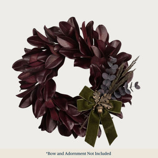 Styled Merlot colored magnolia wreath with a dark green velvet bow and adornments of purple eucalyptus and an acorn decorative piece 