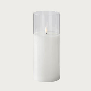 Tall single white LED flickering flameless candle in glass cylinder on minimalist table – battery-powered candlelight for sophisticated home décor.