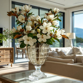 Taupe cut glass vase on clear pedestal filled with white florals in a modern living room with large windows and neutral furnishings, creating an elevated, light-filled interior.
Taupe cut glass vase on pedestal base styled with magnolia branches in a contemporary home setting with natural light and warm neutral tones.