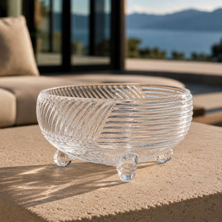 Vintage-inspired clear glass footed bowl displayed on a sculptural limestone table at a contemporary Lake Tahoe estate, with soft golden-hour light and serene mountain views beyond.