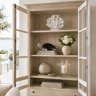 A collected coastal bookshelf vignette featuring the Tranquil Tortoise glass sculpture layered with warm neutrals, sculptural coral, candlelight, and natural textures for a relaxed luxury aesthetic.