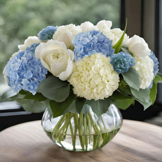 True Bloom Blue Hydrangea Garden Arrangement featuring real touch blue and white hydrangea with white roses displayed in sculpted glass bowl on modern coffee table in light-filled coastal livi