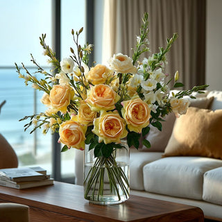26 inch True Bloom real touch yellow Juliet roses arranged with white anemones and soft greenery in a clear glass vase on a modern coastal living room coffee table with ocean view.