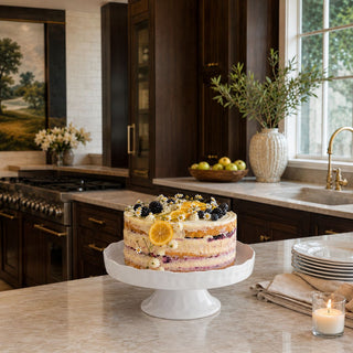 white ceramic footed serving tray styled with layered berry cake on marble kitchen island in luxury kitchen with warm wood cabinetry