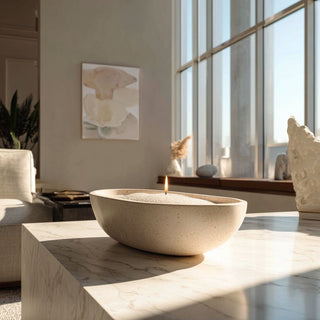 White candle sand styled in a shallow travertine bowl on a marble console table in a contemporary upscale living room with soft morning light