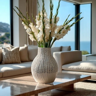 White ceramic latticework vase styled with tall white gladiolus stems on a travertine coffee table in a luxury Malibu modern living room with large windows and coastal daylight