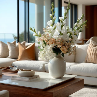 Large floral arrangement featuring white True Bloom real touch gladiolus stems layered with ivory blooms and warm neutral florals, styled in a matte ceramic vase on a modern coffee table in a light-filled living room.
