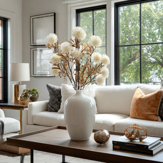 White ceramic vase with multiple faux white spike cactus dahlia stems styled in a modern living room with neutral and warm accents.