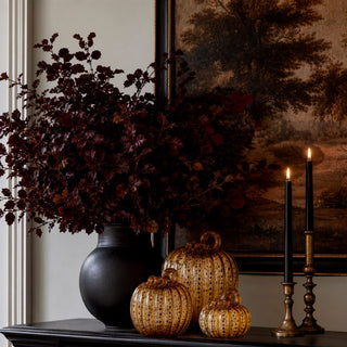Golden amber speckled handblown glass pumpkins styled on a dark console with burgundy branches, brass candlesticks and layered fall decor.