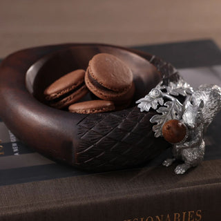 Hartwell dark wood and pewter squirrel nut bowl styled with chocolate treats on stacked books, showing sculpted squirrel, oak leaf, and acorn trim.