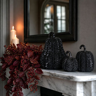 Glossy black resin pumpkins styled as a trio in all three sizes, with raised embossed texture, reflective black finish, and sculptural curved and looped stems for contemporary fall and Halloween decor.