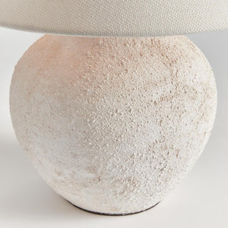 The Theo Table Lamp lit at dusk, textured ceramic body with linen shade casting warm ambient light