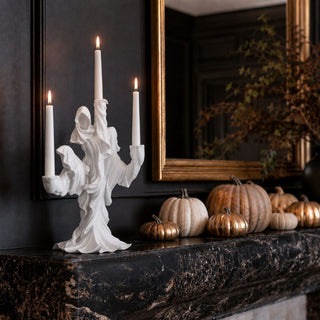 17.5-inch white resin draped ghost three-taper candle holder styled with lit ivory taper candles, neutral and metallic pumpkins, and black marble Halloween decor.